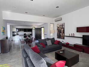 Una sala de estar moderna con un sofá gris, cojines rojos, una mesa de centro y un televisor sobre un mueble.