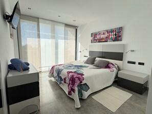Un dormitorio moderno con una cama grande, un televisor de pantalla plana, un cuadro y un escritorio con una toalla.