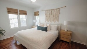 A bedroom with a large bed, two bedside tables, a wall-mounted macrame piece, and a window with blinds. - Ocean Beach House 3BR, Parking, Large Patio, Firepit, Grill and 2 blocks from the beach (San Diego)