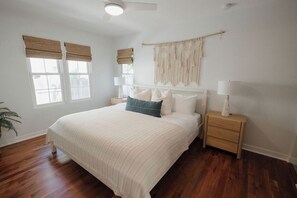 Un dormitorio con una cama grande, dos mesitas de noche, un tapiz de macramé en la pared y una ventana con persianas.