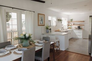Una cocina moderna con armarios blancos, una isla central y un comedor con una mesa blanca dispuesta para cuatro.