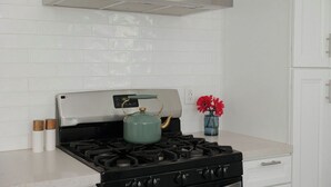 A kitchen with a stainless steel range hood, a gas stove with a green kettle, and a vase with red flowers on the counter. - Ocean Beach House 3BR, Parking, Large Patio, Firepit, Grill and 2 blocks from the beach (San Diego)