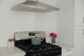 Una cocina con una campana extractora de acero inoxidable, una estufa a gas con un hervidor verde, y un florero con flores rojas sobre la encimera.