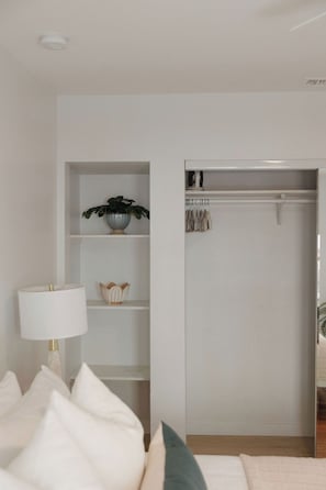 A bedroom with a bed, a bedside lamp, a shelf with decorative items, and a closet. - Ocean Beach House 3BR, Parking, Large Patio, Firepit, Grill and 2 blocks from the beach (San Diego)