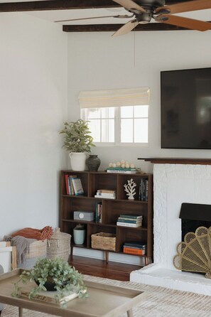 A living room with a fireplace, a bookshelf, and a ceiling fan. - Ocean Beach House 3BR, Parking, Large Patio, Firepit, Grill and 2 blocks from the beach (San Diego)