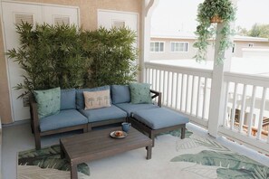 Ein Balkon mit einem blauen Sofa, einem Holztisch und einem Blumentopf.