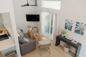A modern living room with a grey sofa, a wooden chair, a coffee table, and a flat-screen TV mounted on the wall. - OB Townhome, 2 blocks to beach with Private Garage (San Diego)