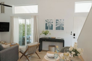 A modern living room with a sofa, a dining table with a vase of flowers, and a TV mounted on the wall. - OB Townhome, 2 blocks to beach with Private Garage (San Diego)