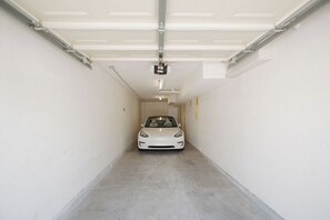 A car parked in a garage with a ceiling light fixture and a garage door. - Heart of OB, Walk to Beach, Townhome with Garage and Patio (San Diego)