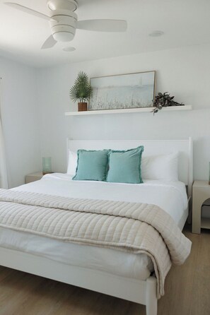 A bedroom with a bed, a ceiling fan, a nightstand, a bedside table, and a wall-mounted shelf with a plant. - Heart of OB, Walk to Beach, Townhome with Garage and Patio (San Diego)