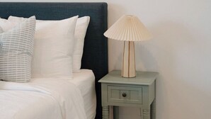 Un dormitorio con cama, almohadas, una mesita de noche con lámpara y decoración en la pared.