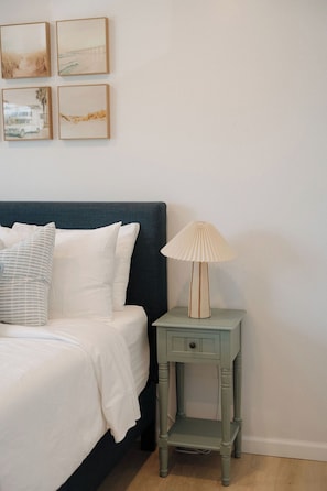 A bedroom with a bed, pillows, a bedside table with a lamp, and wall art. - Heart of OB, Walk to Beach, Townhome with Garage and Patio (San Diego)