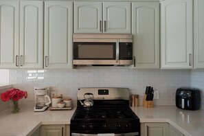A kitchen with white cabinets, a stainless steel microwave, a gas stove, a coffee maker, and an air fryer. - Heart of OB, Walk to Beach, Townhome with Garage and Patio (San Diego)