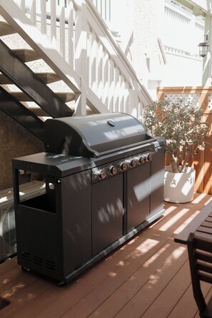 Ein Grill mit Bedienfeld, platziert auf einer Holzterrasse mit einem weißen Zaun und einem Blumentopf im Hintergrund.