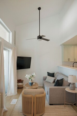 A modern living room with a ceiling fan, a flat-screen TV, a sofa, a coffee table, and a lamp. - Heart of OB, Walk to Beach, Townhome with Garage and Patio (San Diego)