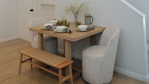 Un comedor con mesa de madera, sillas y banco. Se ve una escalera al fondo.