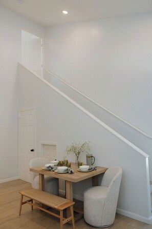 A dining area with a wooden table, chairs, and a bench. A staircase is visible in the background. - Heart of OB, Walk to Beach, Townhome with Garage and Patio (San Diego)