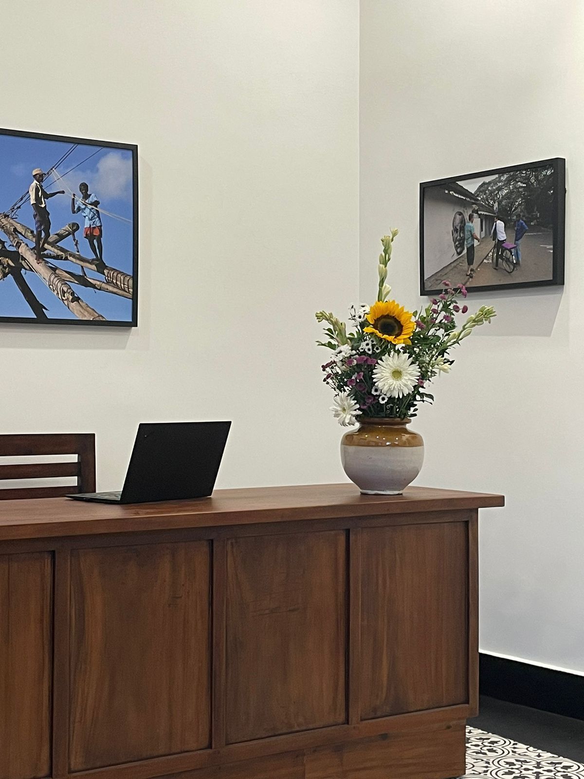Un comptoir d’accueil en bois, sur lequel se trouvent un ordinateur portable, un vase de fleurs et deux photographies encadrées accrochées au mur.