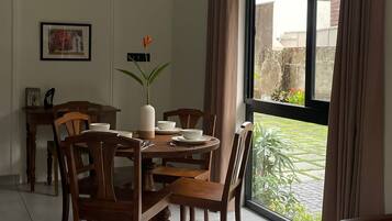 A dining area with a round table, chairs, a vase with flowers, and a window with curtains.