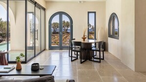 Una habitación amplia con un gran ventanal corredero que da a una piscina, una mesa redonda con sillas y vistas al exterior.