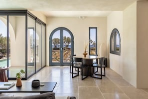 A spacious room with a large sliding glass door leading to a pool, a round table with chairs, and a view of the outdoors. - Exomitis1 Cellar & Sea Escape (8CMR+3XX Exomitis, Greece)