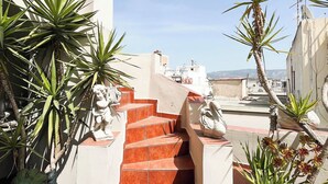 A rooftop terrace with red-tiled stairs, potted plants, and white walls.