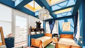A room with two beds, a large window, a decorative ceiling light, and a view of the city.