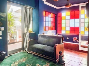 Una habitación con un sofá, una planta en maceta, un ventanal con vidrio de colores y un ventilador de techo.