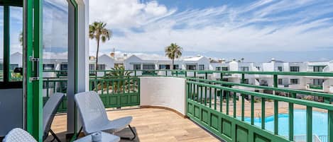 Un balcon avec des fauteuils en osier et vue sur la piscine.