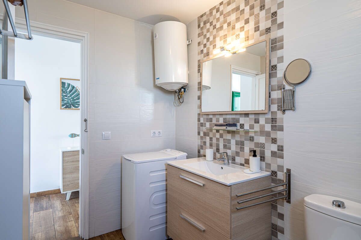 Un baño con lavamanos blanco, espejo, toallero, inodoro y calefactor.