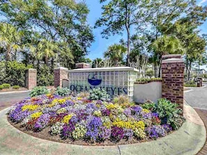 A sign with "OCEAN KEYES" and a colorful flower bed in front. - 3 bedroom in gated community. Walk to the beach. (North Myrtle Beach)