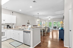 A modern kitchen with white cabinetry, a central island, and a dining area with a view. - 3 bedroom in gated community. Walk to the beach. (North Myrtle Beach)