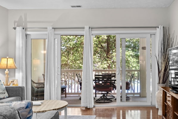 A living room with a sofa, a small table, a lamp, and a TV. There is a sliding glass door leading to an outdoor patio with chairs and a table. - 3 bedroom in gated community. Walk to the beach. (North Myrtle Beach)