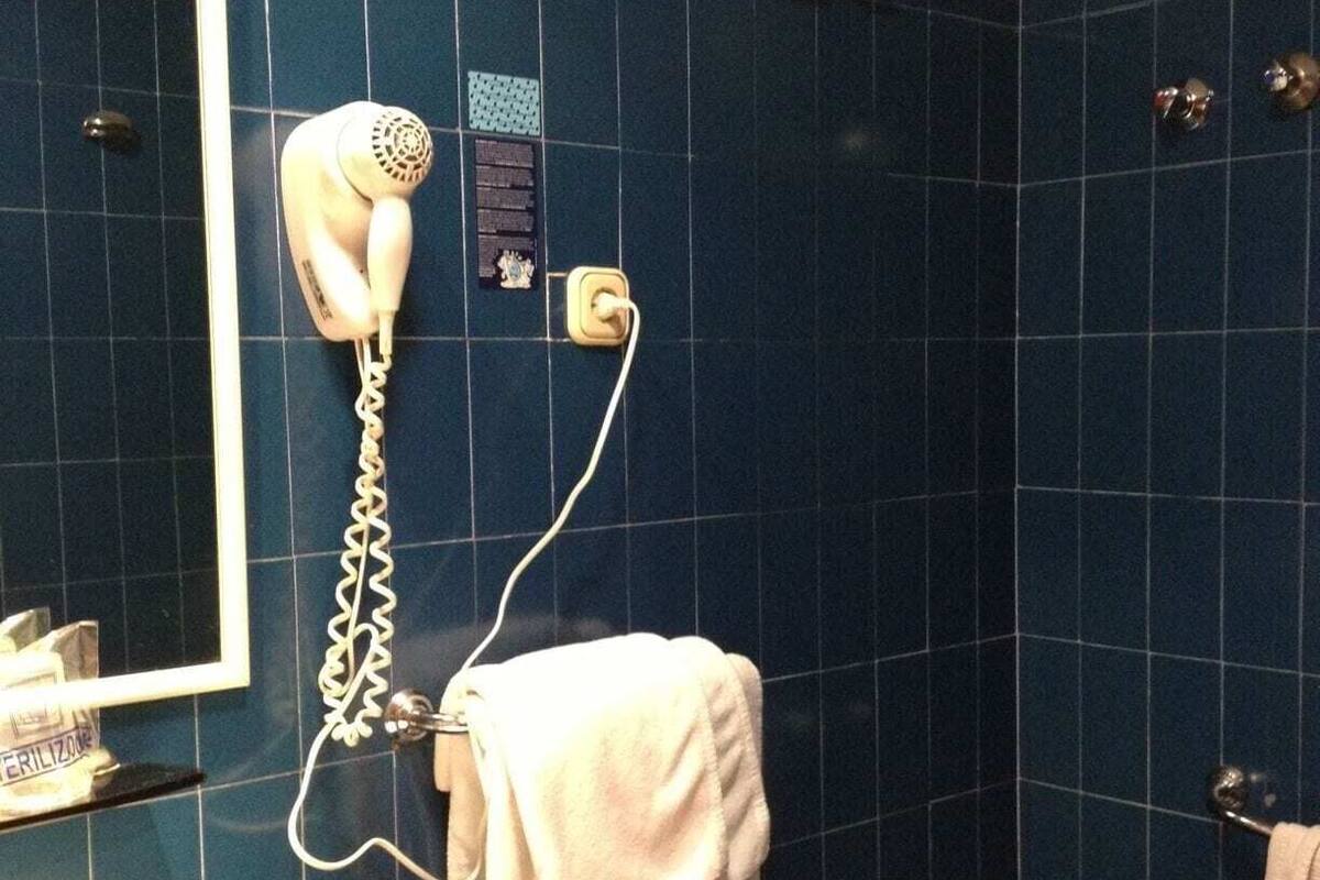 A bathroom with a blue tiled wall, a white sink, a bidet, and a hairdryer mounted on the wall.