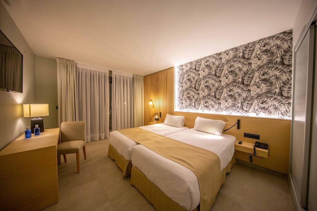 A hotel room with a bed, a desk, a chair, a lamp, and a wall with a patterned design.