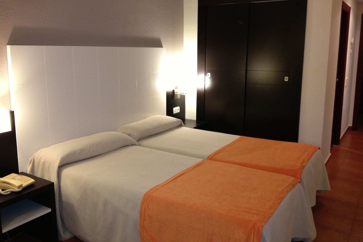 A hotel room with a bed, a nightstand, a telephone, a wardrobe, and a wall-mounted light.