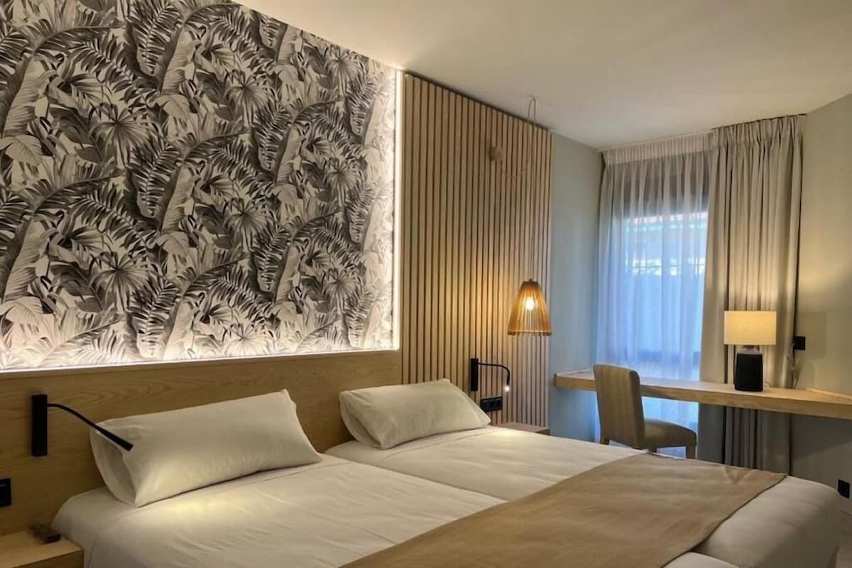 A hotel room with a large bed, a desk, a chair, a lamp, and a wall with a leaf pattern.