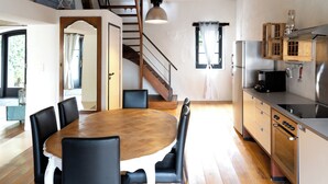 Comedor con mesa y sillas de madera, cocina con electrodomésticos de acero inoxidable y una escalera que sube a otro nivel.