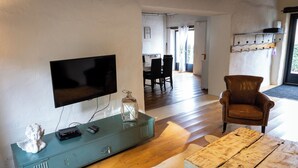 Una sala de estar con televisor, un mueble azul, un sillón de cuero y una mesa de centro de madera.