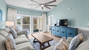 Una sala de estar con ventilador de techo, televisor, un mueble azul y un sofá con cojines estampados.