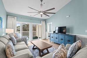 Ein Wohnzimmer mit Deckenventilator, Fernseher, einem blauen Schrank und einer Couch mit gemusterten Kissen.