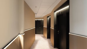 A hallway with carpeted floors, beige walls, and black doors with illuminated interiors. - Limehome Bilbao Deusto (Bilbao)