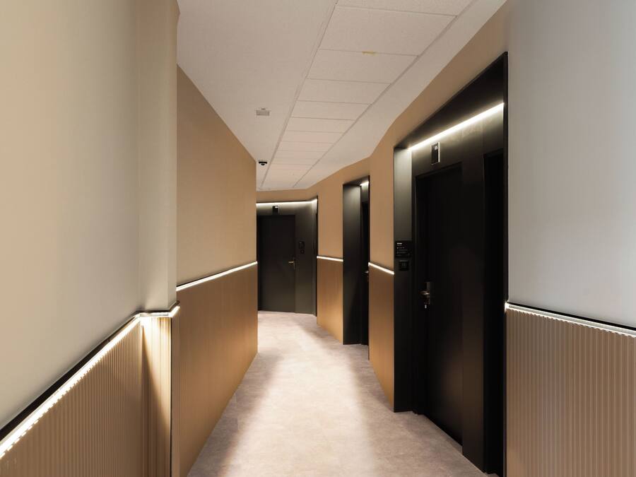 Un pasillo con pisos alfombrados, paredes color crema y puertas negras con interiores iluminados.