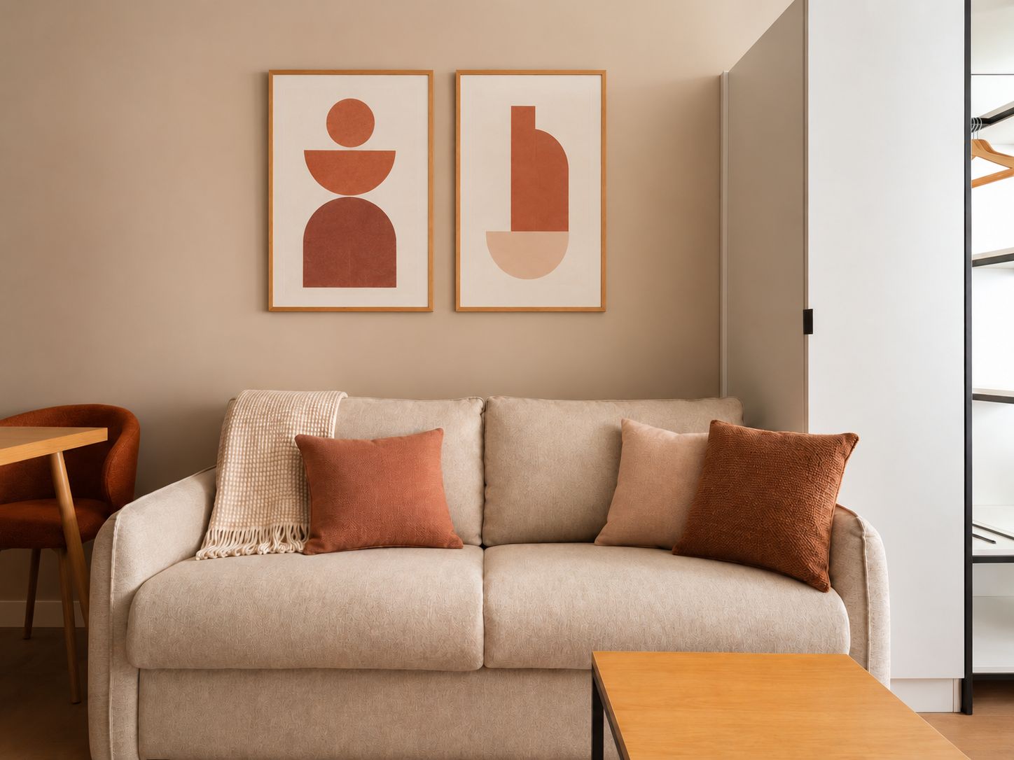 Un salon aux couleurs neutres, comprenant un canapé, deux coussins, une table basse en bois et deux œuvres d’art abstraites encadrées accrochées au mur.