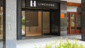A modern building entrance with a 'LIMEHOME' sign, a glass door, and a small outdoor area with plants. - Limehome Bilbao Deusto (Bilbao)