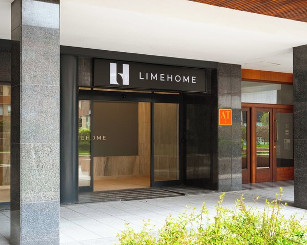 A modern building entrance with a 'LIMEHOME' sign, a glass door, and a small outdoor area with plants.