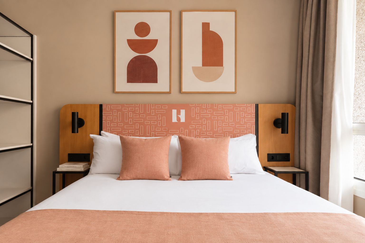 Une chambre d’hôtel avec un lit, deux oreillers, une tête de lit ornée d’un motif géométrique, une œuvre d’art accrochée au mur et une table de chevet avec une lampe.