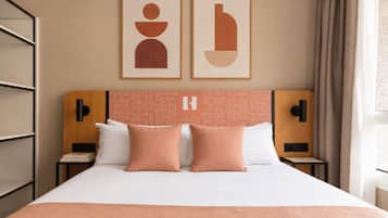 Une chambre d’hôtel avec un lit, deux oreillers, une tête de lit ornée d’un motif géométrique, une œuvre d’art accrochée au mur et une table de chevet avec une lampe.