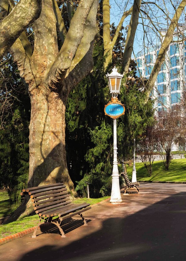 A park bench, a lamppost with a sign, and a tree. - Limehome Bilbao Deusto (Bilbao)