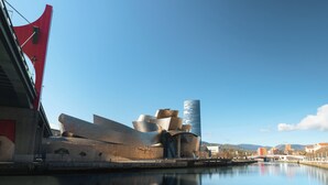 A modern architectural structure with a reflective surface, a bridge, and a calm body of water. - Limehome Bilbao Deusto (Bilbao)